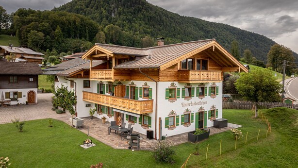 Un bâtiment traditionnel en bois, doté d’un balcon, d’une terrasse en pierre et offrant une vue sur une montagne boisée.