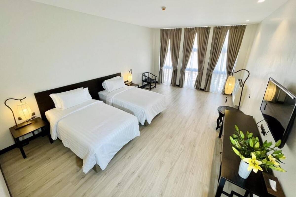 A hotel room with two beds, a desk, a chair, and a potted plant.
