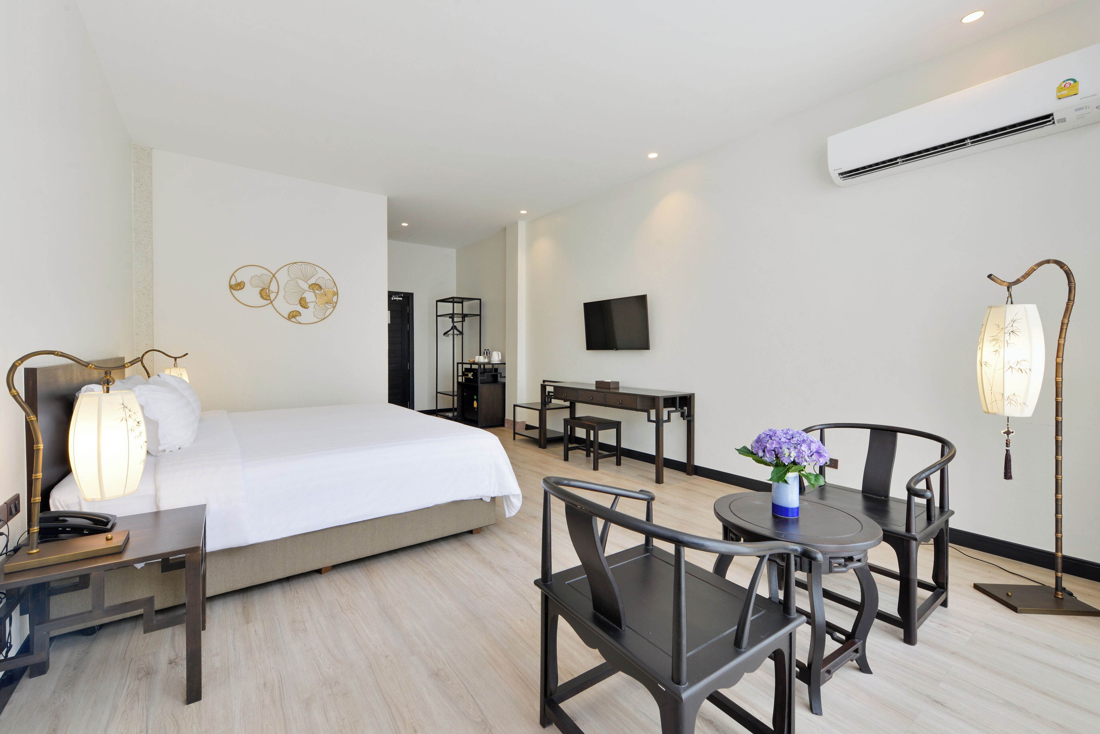 A hotel room with a bed, bedside table, lamp, desk, chair, and a small table with a vase of flowers.