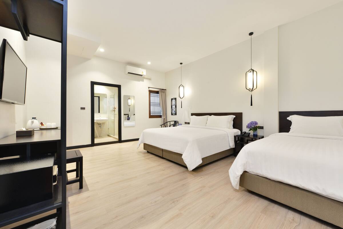 A hotel room with two beds, a desk, a chair, a TV, and a bathroom visible through an open door.