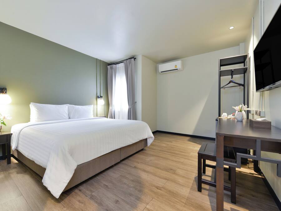 Una habitación de hotel con cama, mesita de noche, lámpara, aire acondicionado y un escritorio con silla.