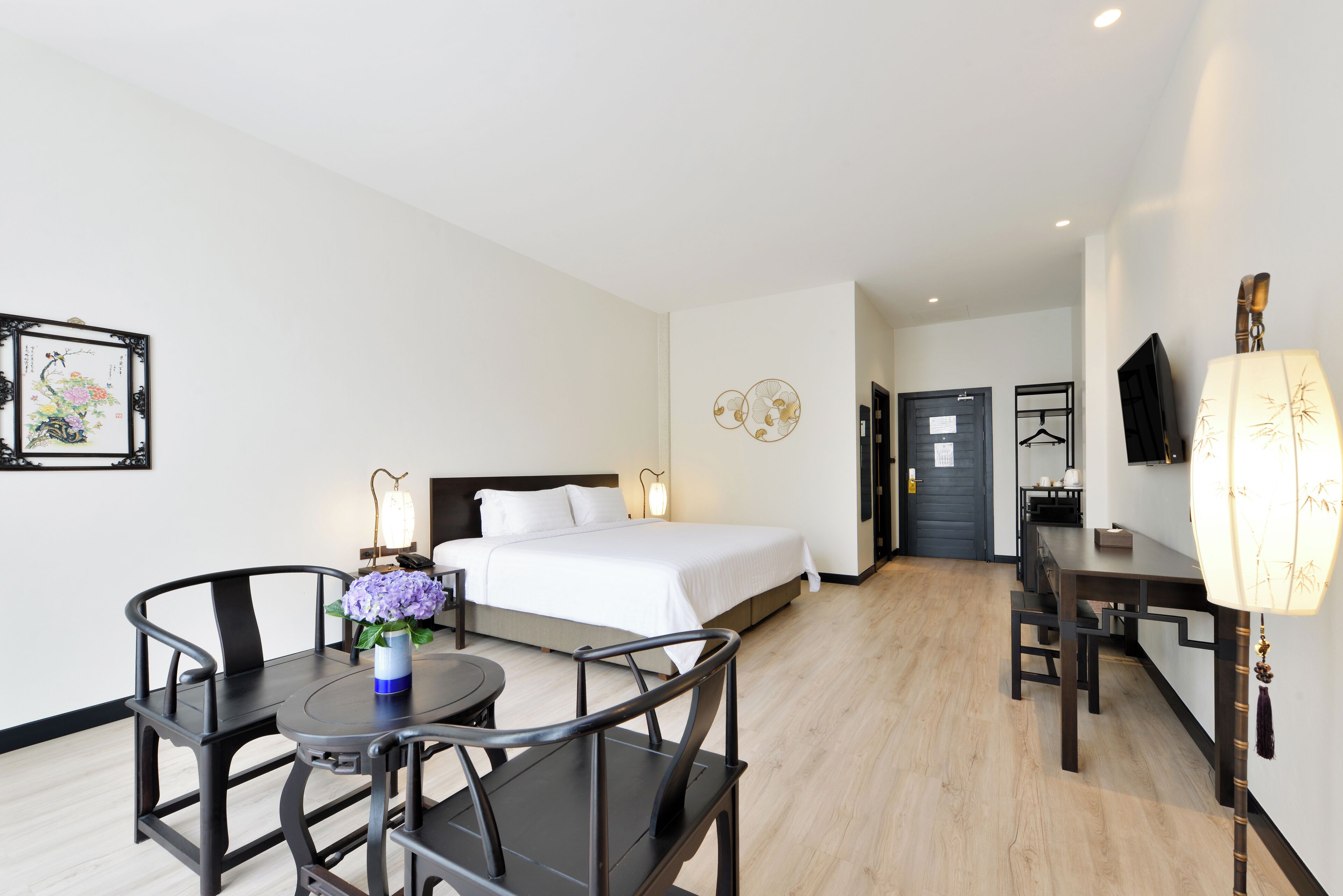 A hotel room with a bed, bedside table, lamp, and a dining area with chairs and a table.