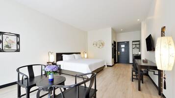 A hotel room with a bed, bedside table, lamp, and a dining area with chairs and a table.