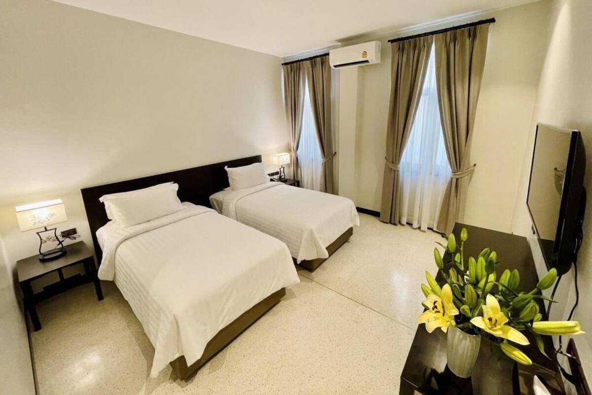A hotel room with two beds, a TV, a desk with a lamp, and a vase with flowers.