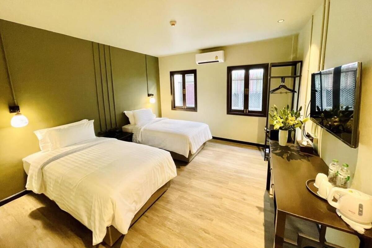 A hotel room with two beds, a desk with a chair, a TV, and a small table with a plant and bottles.