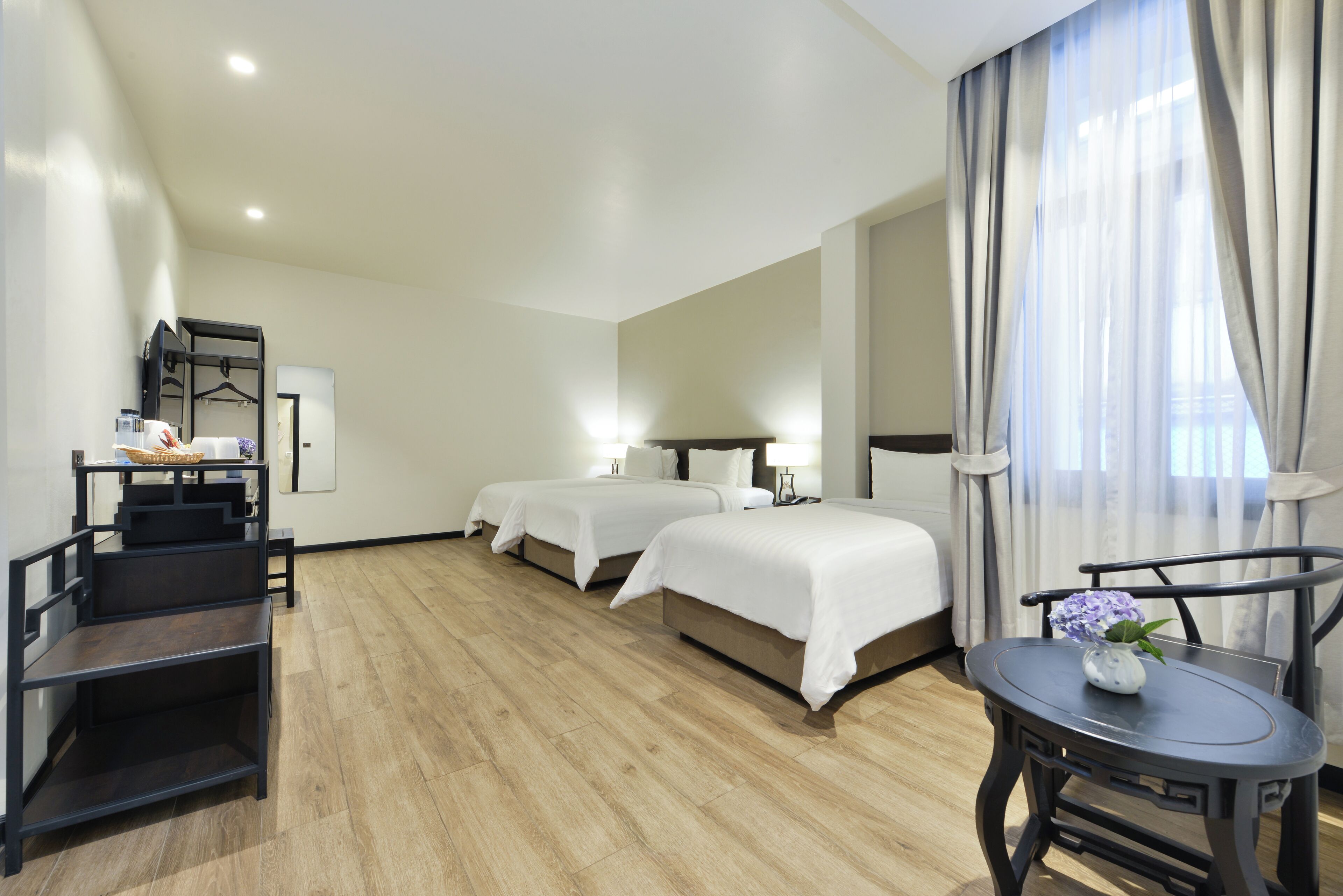 A hotel room with two beds, a desk, a chair, and a small table with a vase of flowers.