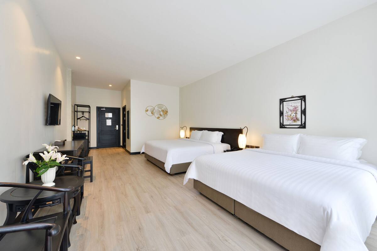 A hotel room with two beds, a desk, and a chair. There is a TV mounted on the wall and a framed picture above the bed.