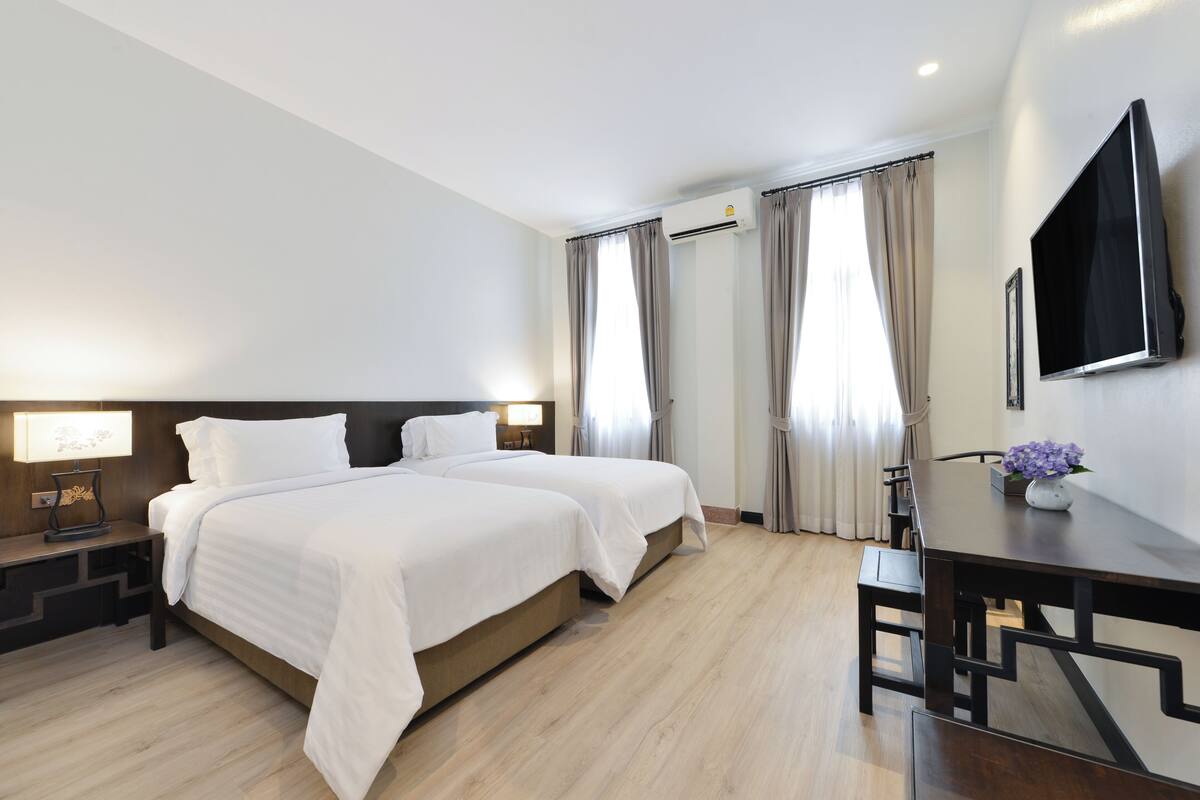 A hotel room with two beds, a desk, a TV, and a window with curtains.