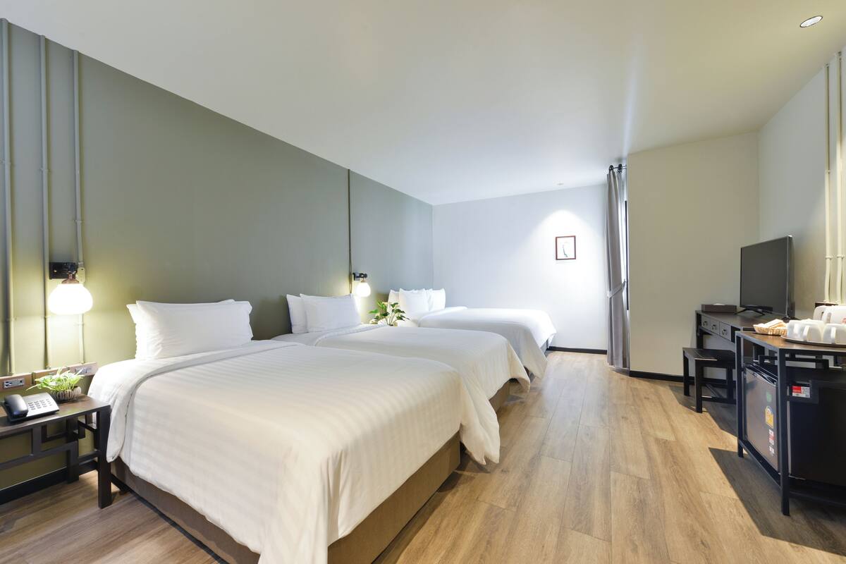 A hotel room with two beds, a desk with a telephone, a television, and a small refrigerator.