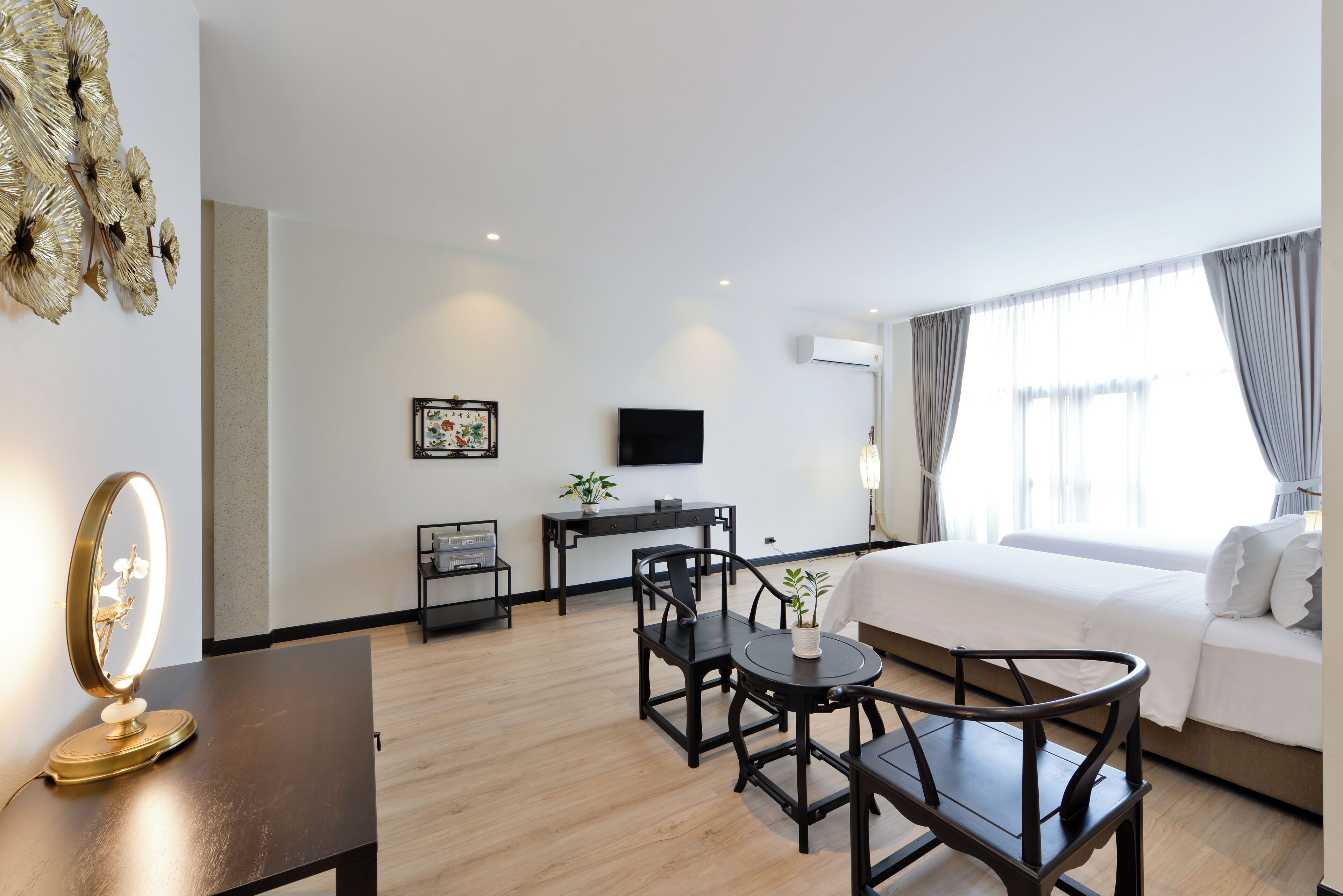 Habitación de hotel con cama, escritorio con silla, una mesita con otra silla, espejo, televisor en la pared y ventana con cortinas.
