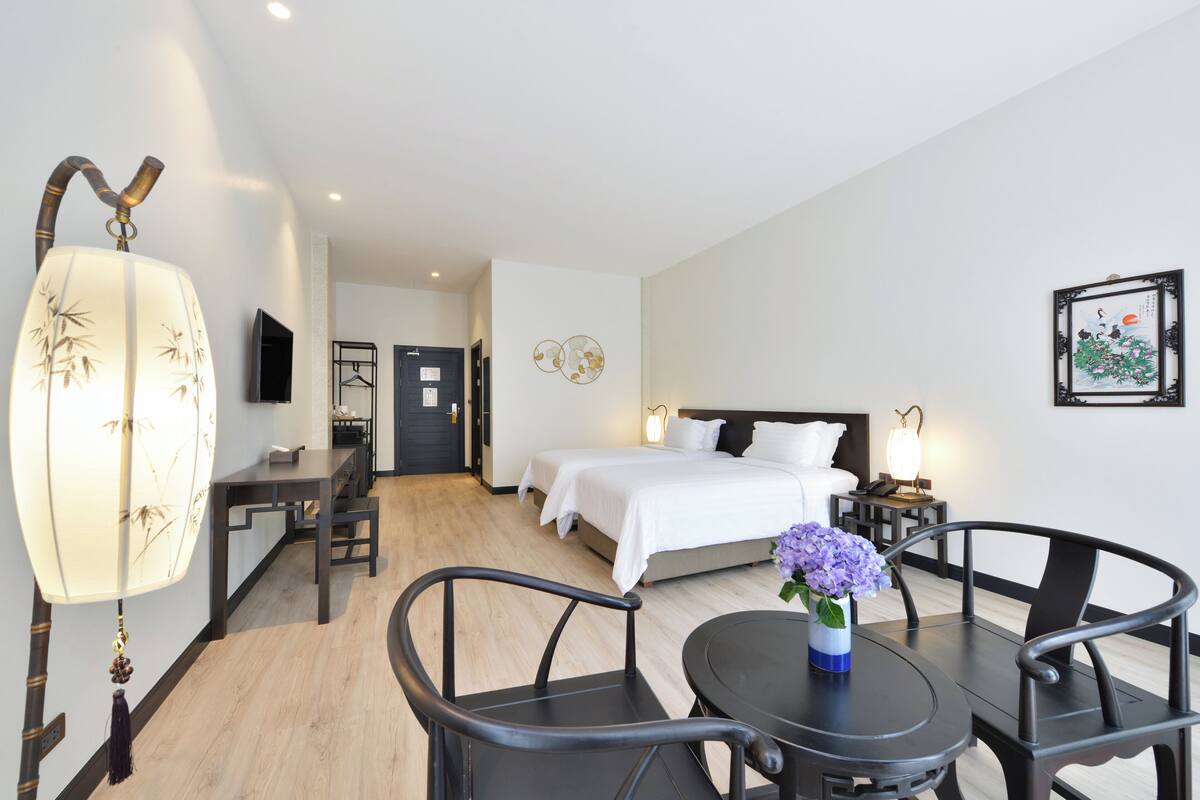 A hotel room with a bed, bedside table, lamp, and a dining area with chairs and a table.