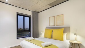 A modern hotel room with a large bed, two bedside lamps, a window with a view, and a cityscape visible through the window. - Bridgewater View 502 (Cape Town)