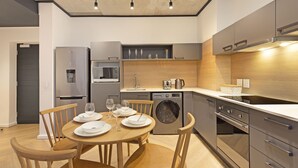 A modern kitchen with a dining area, stainless steel appliances, wooden chairs, and a built-in washing machine. - Bridgewater View 502 (Cape Town)