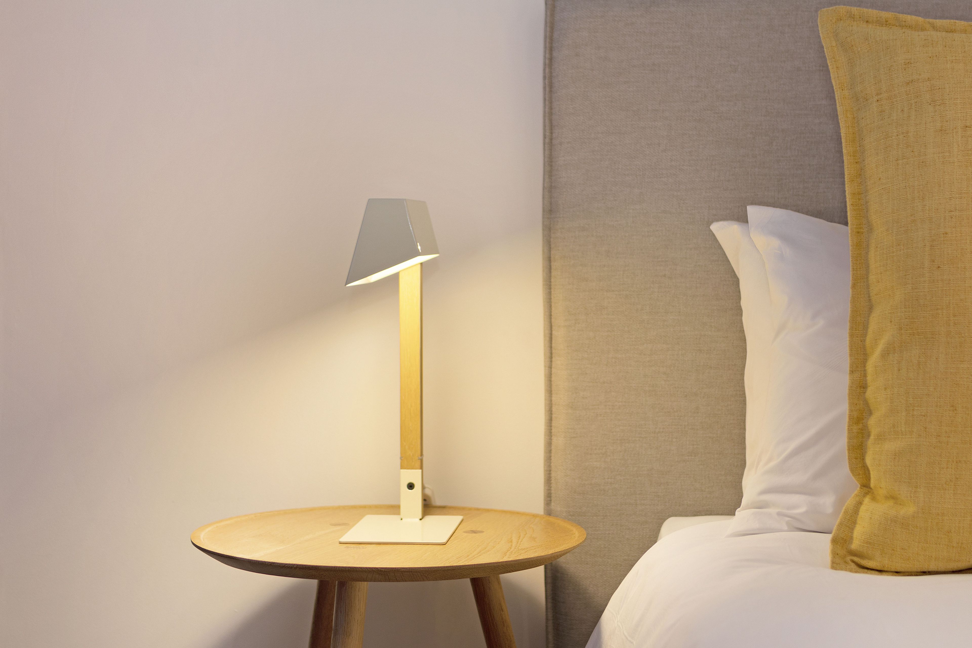 Eine moderne Lampe auf einem Holznachttisch neben einem Bett mit weißen und gelben Kissen.