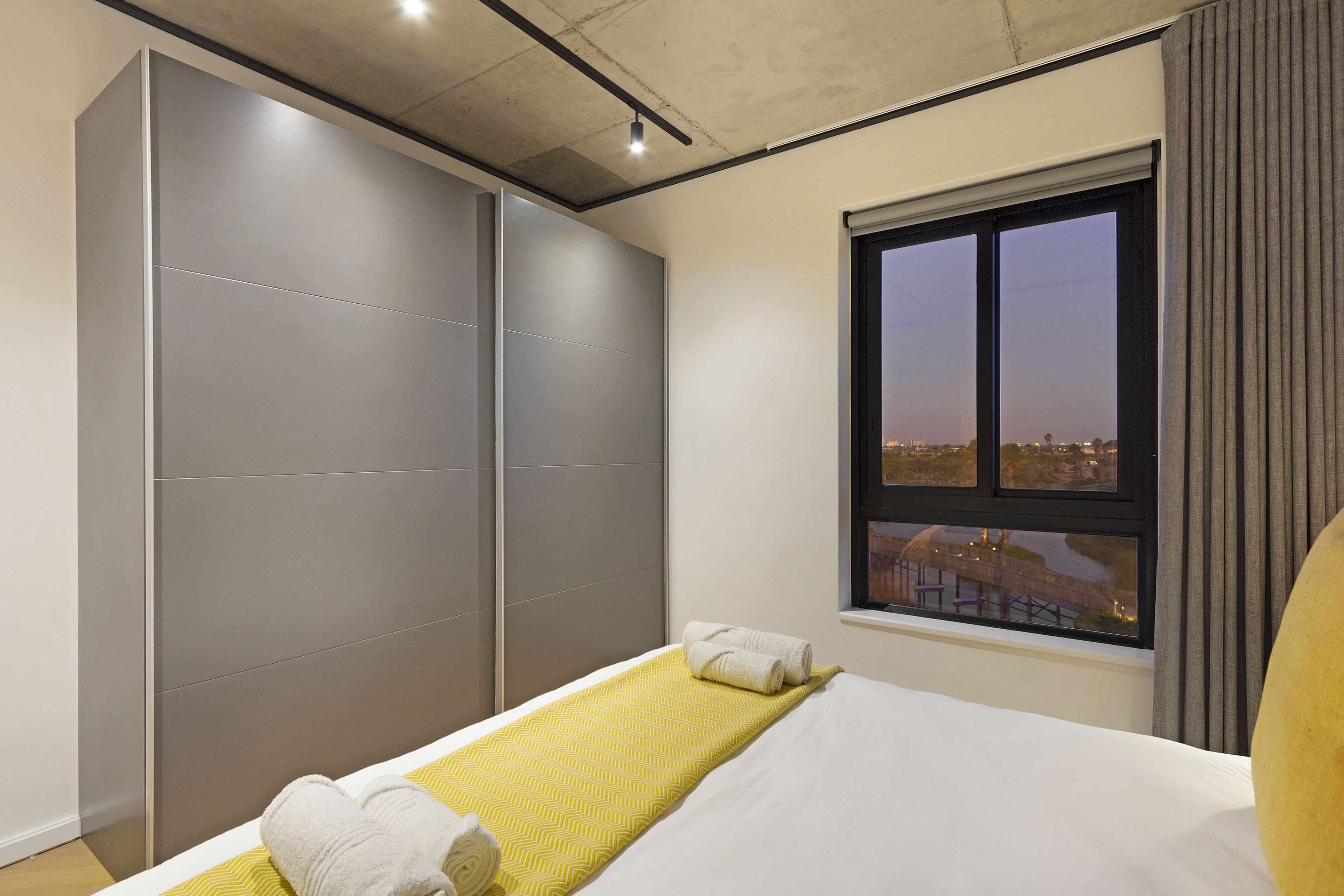 Une chambre moderne avec un lit, une grande armoire et une fenêtre donnant sur la ville.