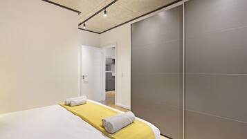 A modern hotel room with a bed, a yellow bedspread, a grey towel, and a sliding door to the bathroom.
