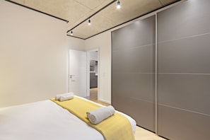 A modern hotel room with a bed, a yellow bedspread, a grey towel, and a sliding door to the bathroom. - Bridgewater View 502 (Cape Town)