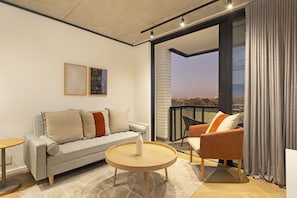 A modern living room with a sofa, armchair, round coffee table, and artwork on the wall. - Bridgewater View 502 (Cape Town)