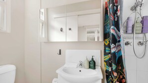 A bathroom with a white sink, a mirror above it, and a shower area with a colorful shower curtain. - Location and lifestyle in a cute luxe studio with stunning city views (Woolloomooloo)