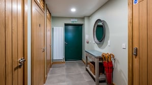 Un couloir avec des portes en bois, une porte de sortie verte, un miroir et une table avec des parapluies.