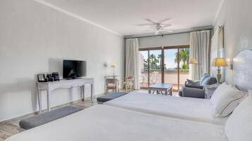 Habitación de hotel con dos camas, televisión, escritorio y balcón con mesa y sillas.