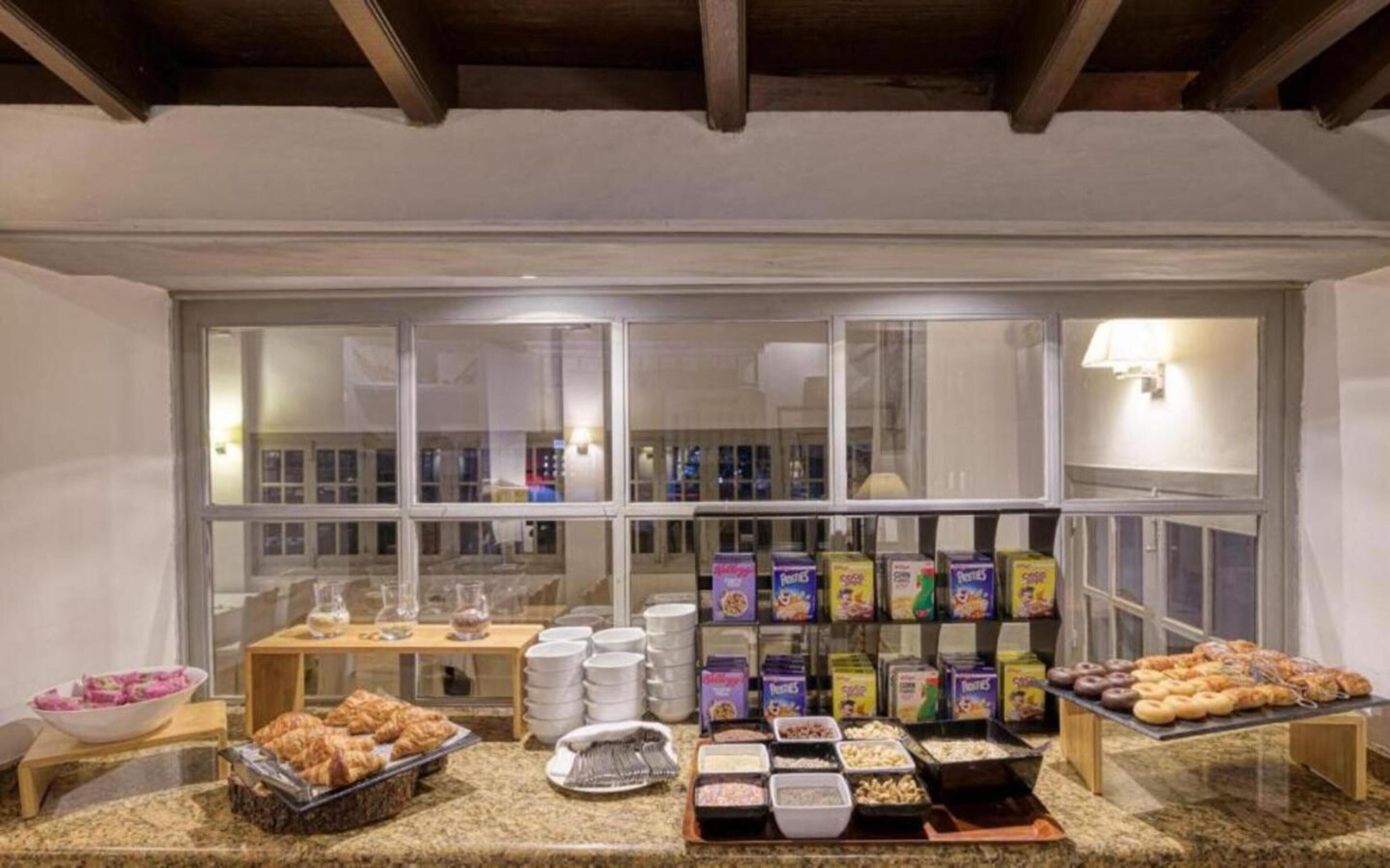 A breakfast buffet with various food items and containers, a window with reflections, and a wooden ceiling.