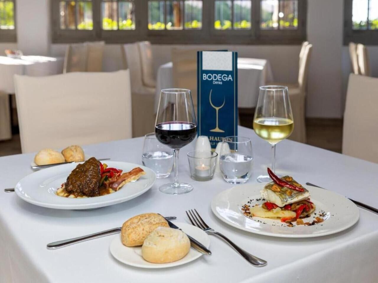 A dining table with plates of food, glasses of wine, and a menu stand.