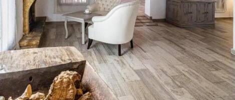 Un salon spacieux avec des poutres apparentes, une cheminée, un fauteuil blanc et un téléviseur.