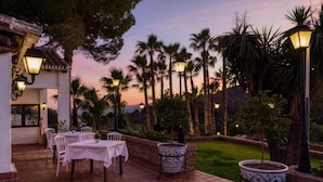 An outdoor patio area with tables and chairs, surrounded by palm trees and a view of the mountains. - Hotel Alhaurín Golf Resort (Alhaurin el Grande)