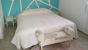A bedroom with a bed, a nightstand, a chair, and a geometric wall design. - Le Petit Gîte du Mont, gîte at the gates of Mont Saint Michel (Beauvoir)