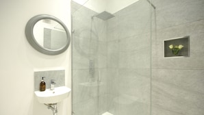 Ein modernes Badezimmer mit einer gläsernen Duschkabine, einem weißen Waschbecken mit Seifenspender und einem Spiegel.