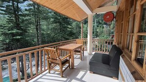 A wooden deck with a table and chairs, a black sofa, and a red hanging object. - Hotel Purnima River View (Bhuntar)
