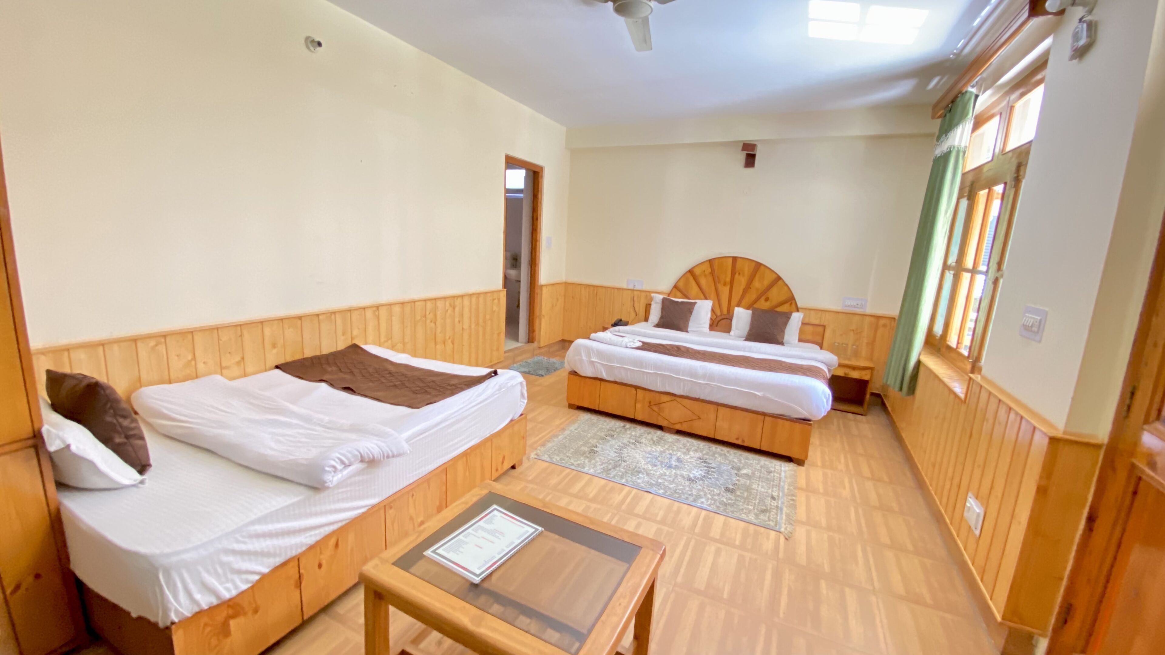 Una habitación con dos camas de madera, una mesita y un ventilador de techo.