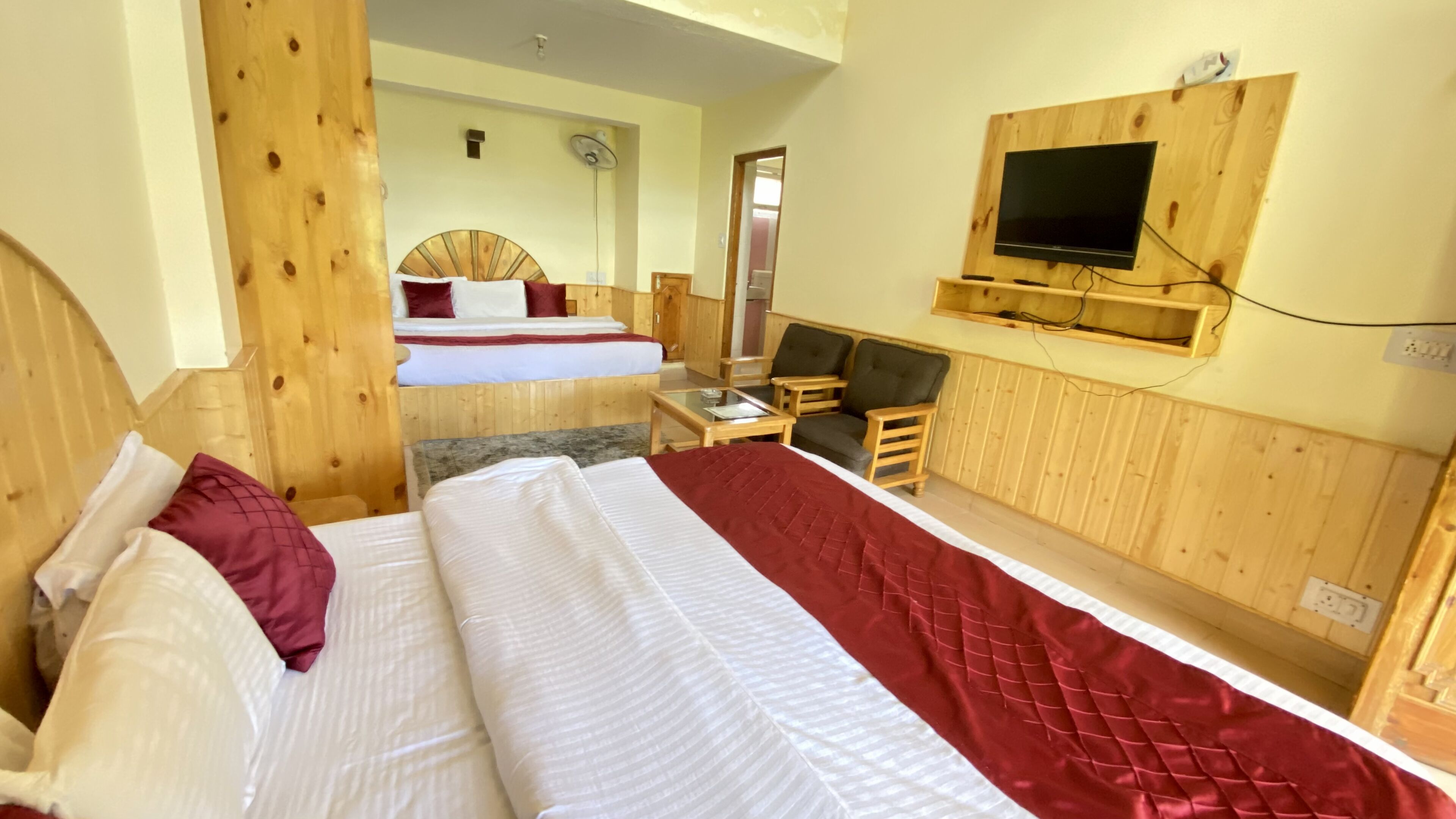 A hotel room with two beds, a TV mounted on the wall, and wooden paneling.