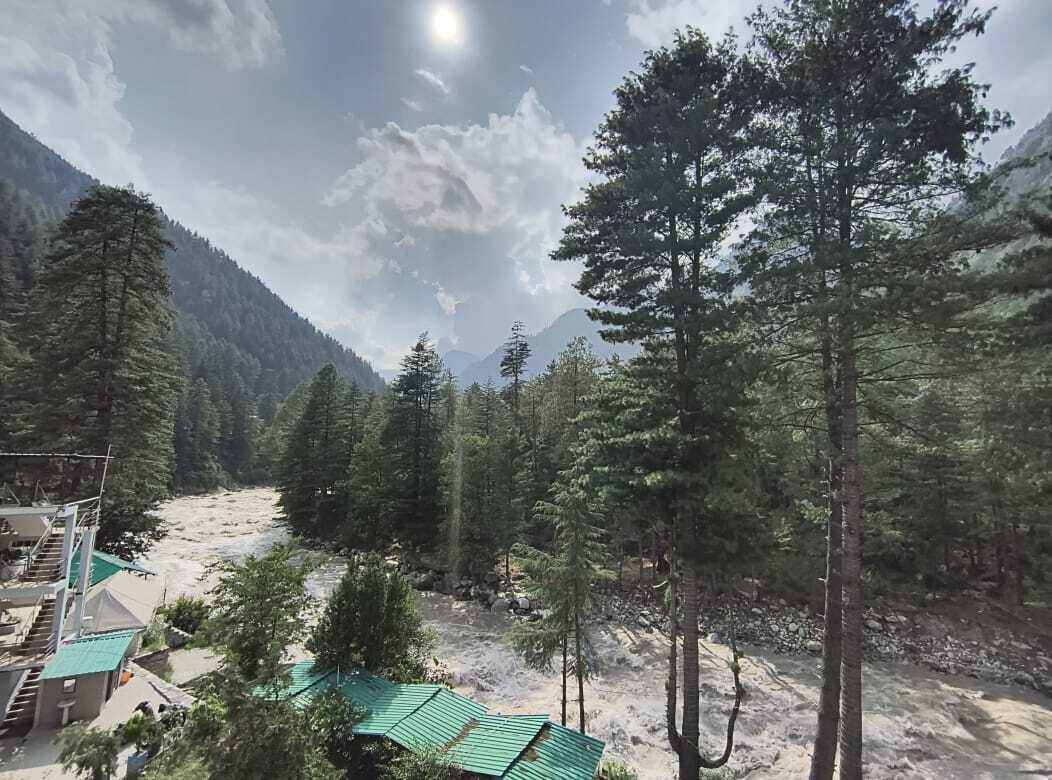 A mountainous landscape with a river, dense forest, and a building with a green roof.