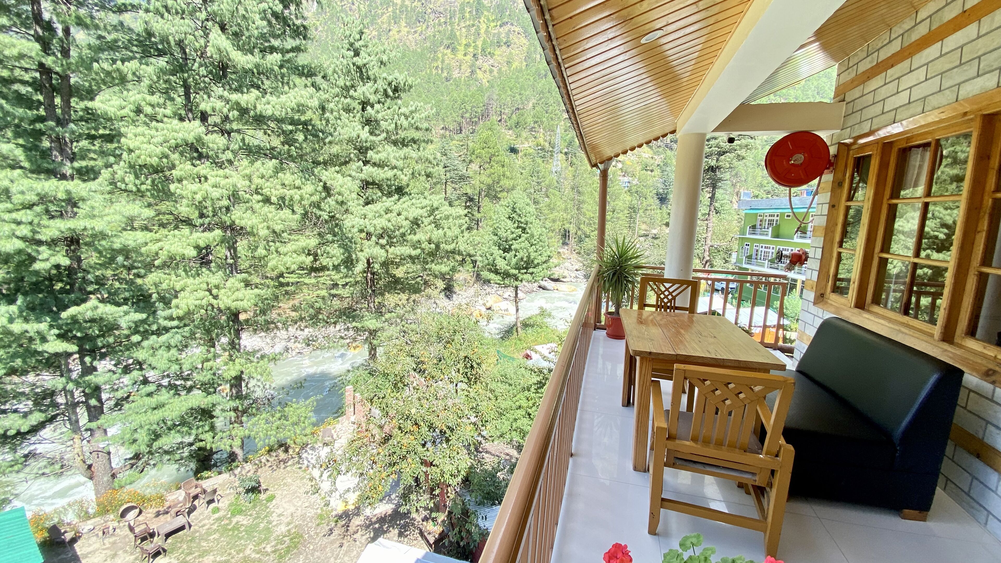 A balcony with a wooden table and chairs, overlooking a river and dense forest.