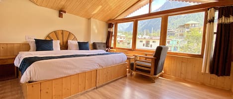 A wooden room with a bed, a chair, and large windows offering a mountain view.