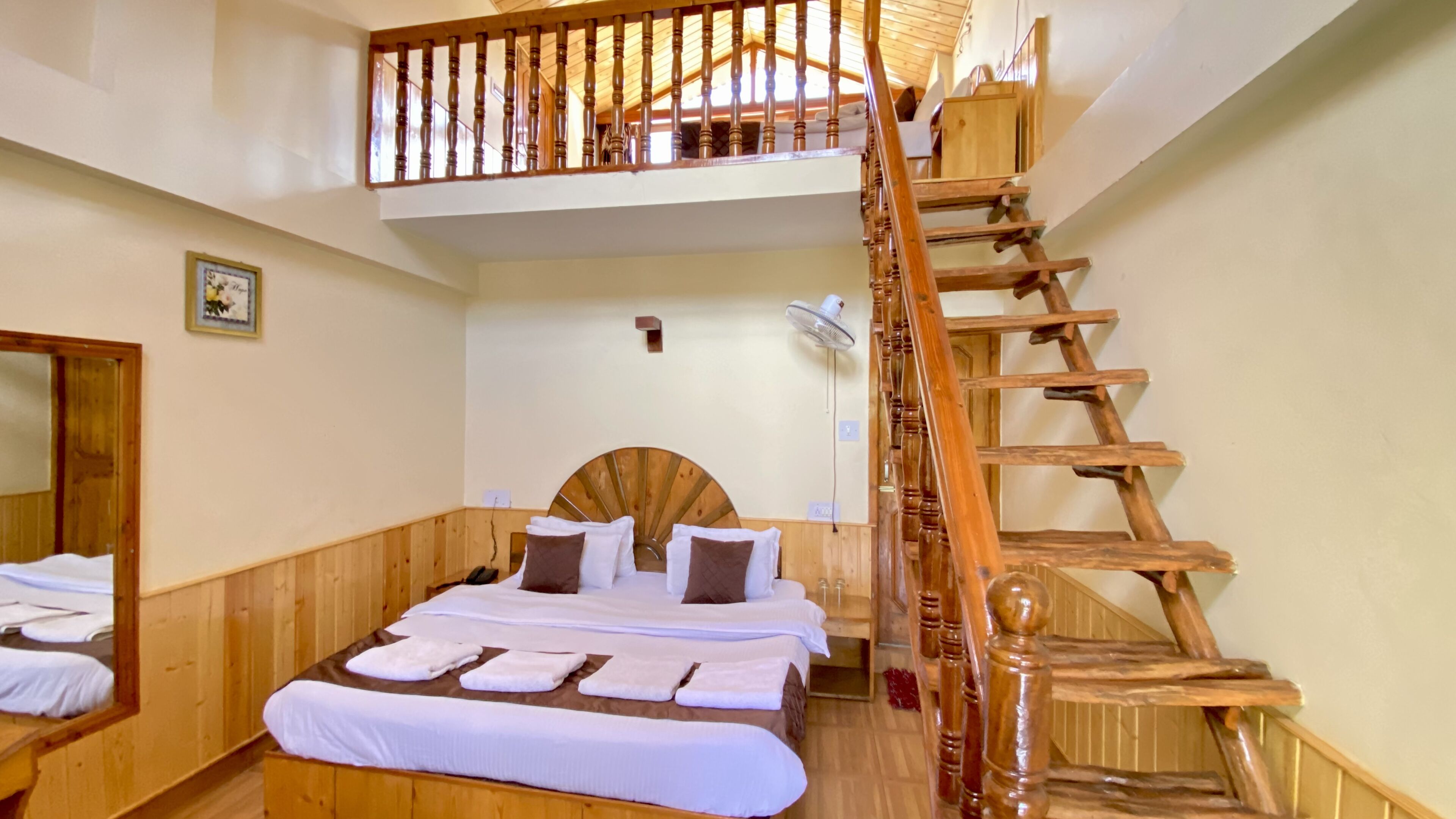 A hotel room with a wooden bed, a large mirror, a wooden staircase, and a ceiling fan.