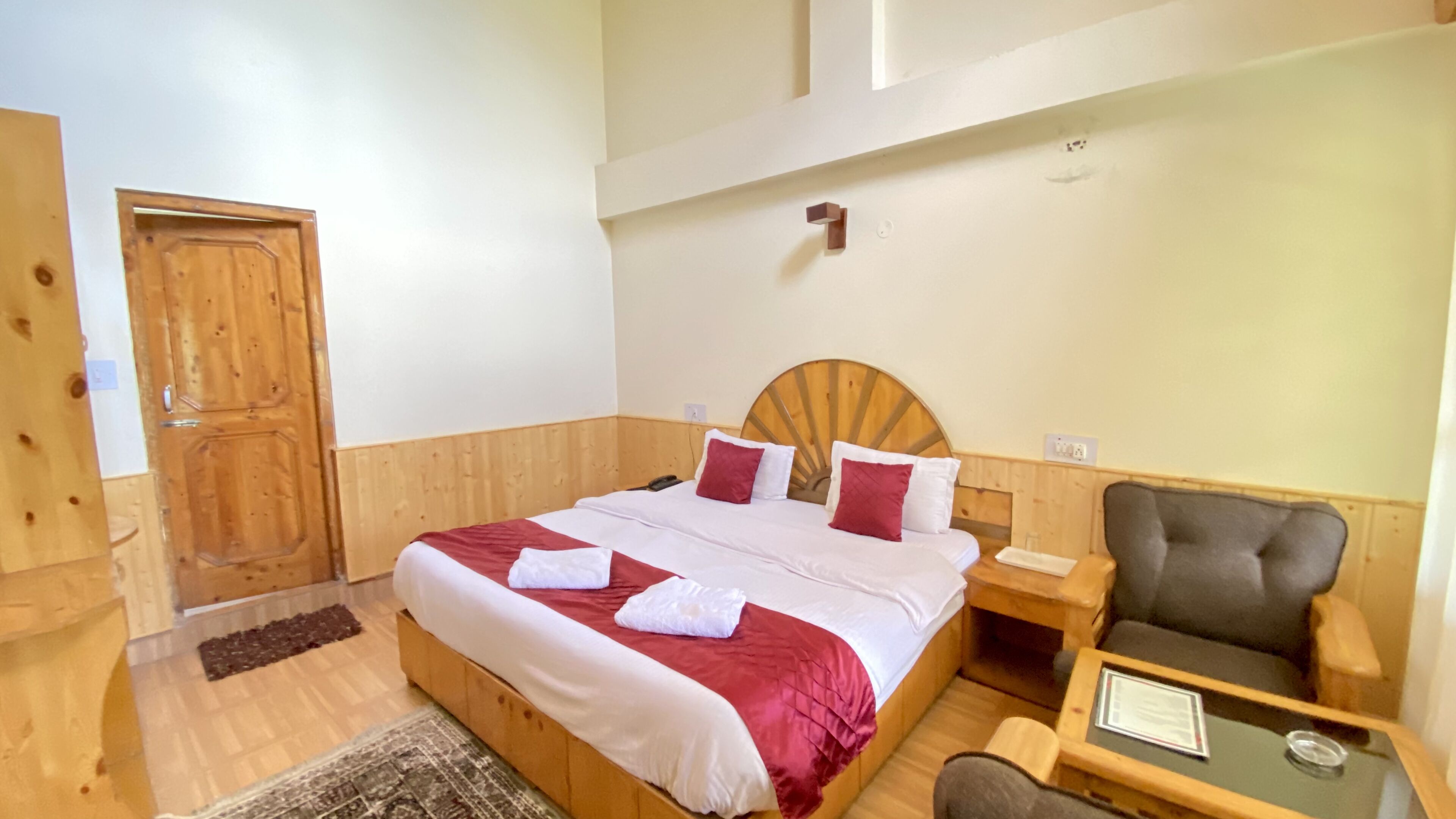 A wooden-framed bedroom with a bed, a chair, a nightstand, and a small table.