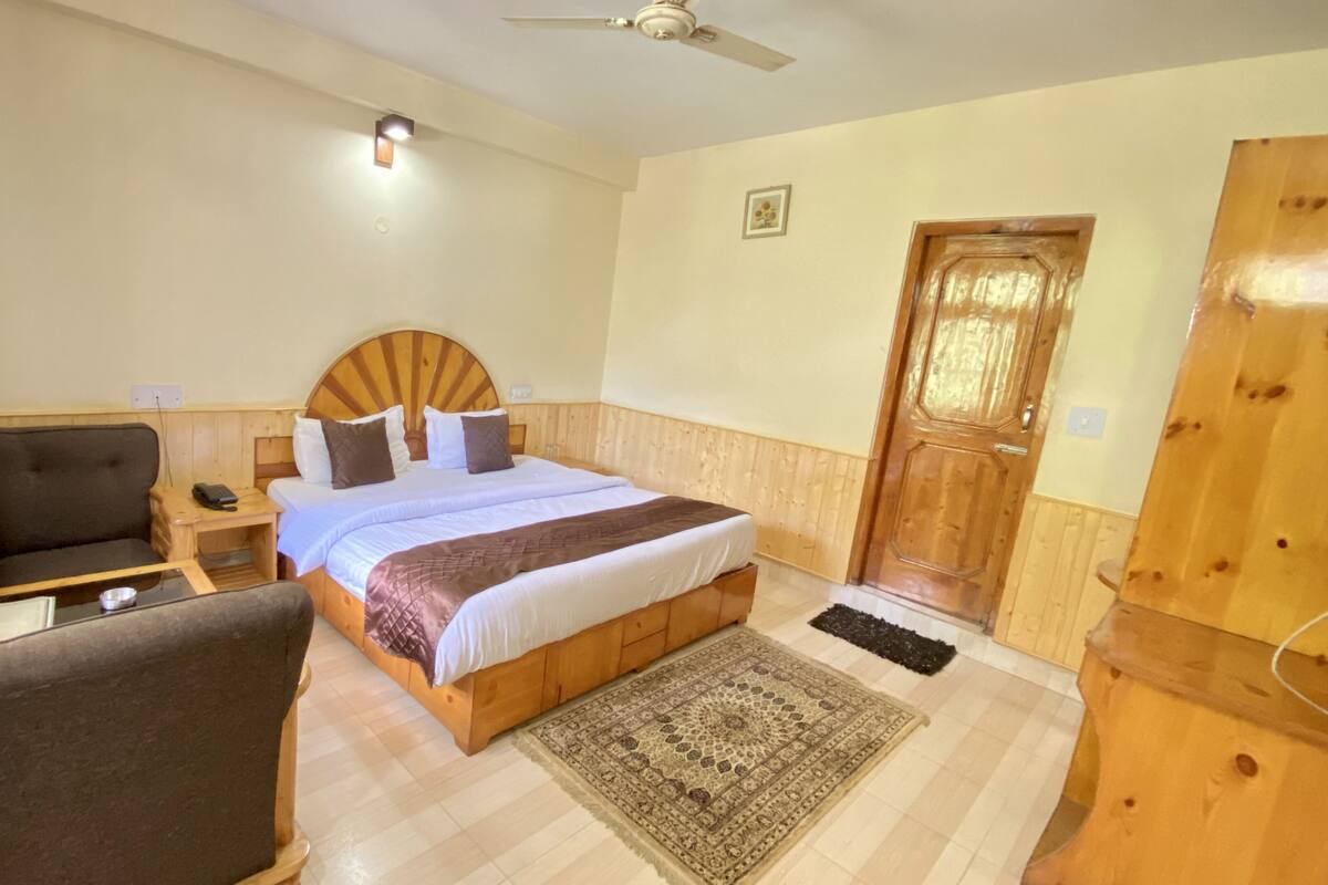 A hotel room with a bed, a desk, a chair, a wooden wardrobe, and a ceiling fan.