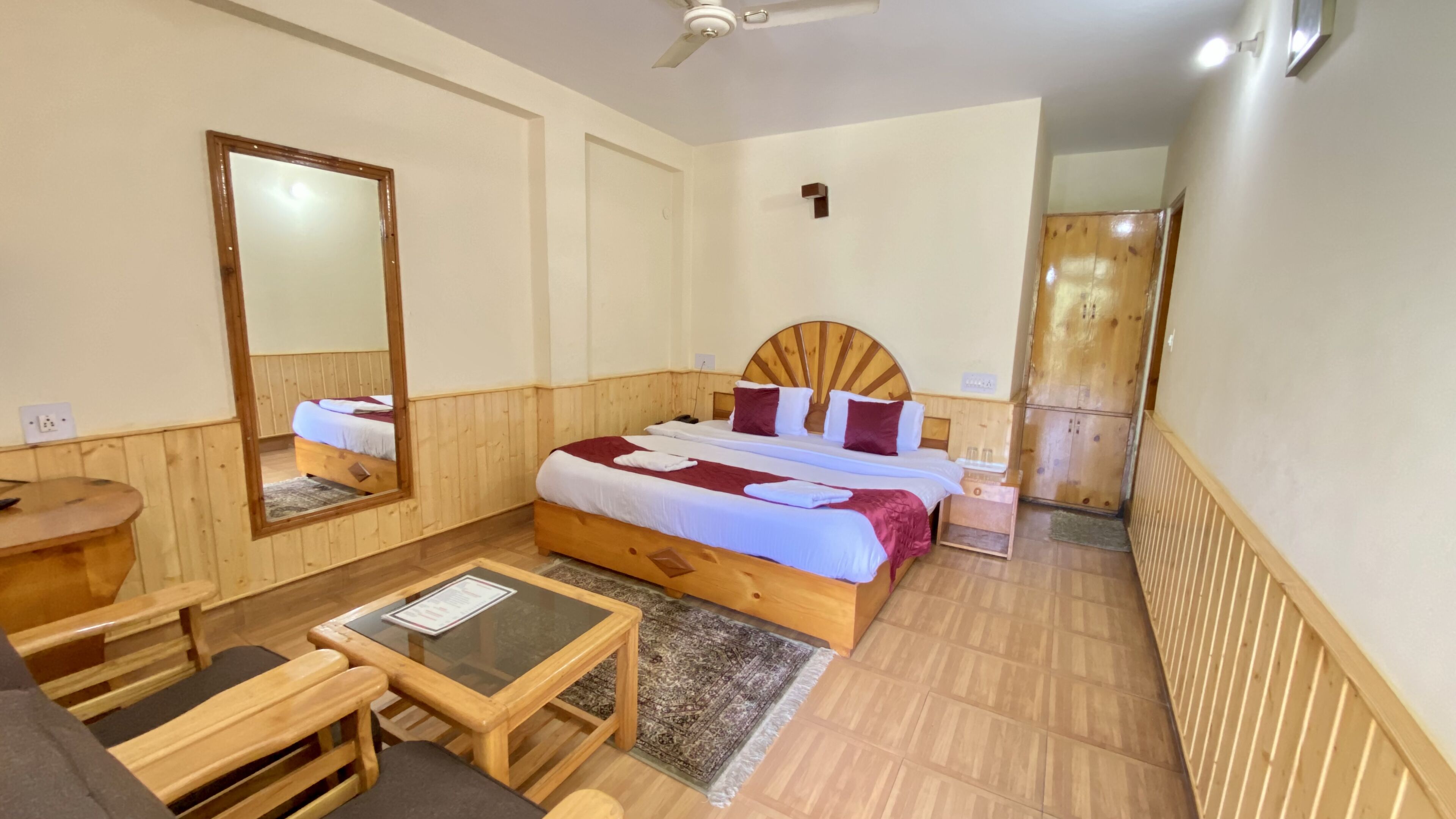 Ein Hotelzimmer mit einem hölzernen Bett, einem kleinen Tisch, einem Spiegel und einem Kleiderschrank.