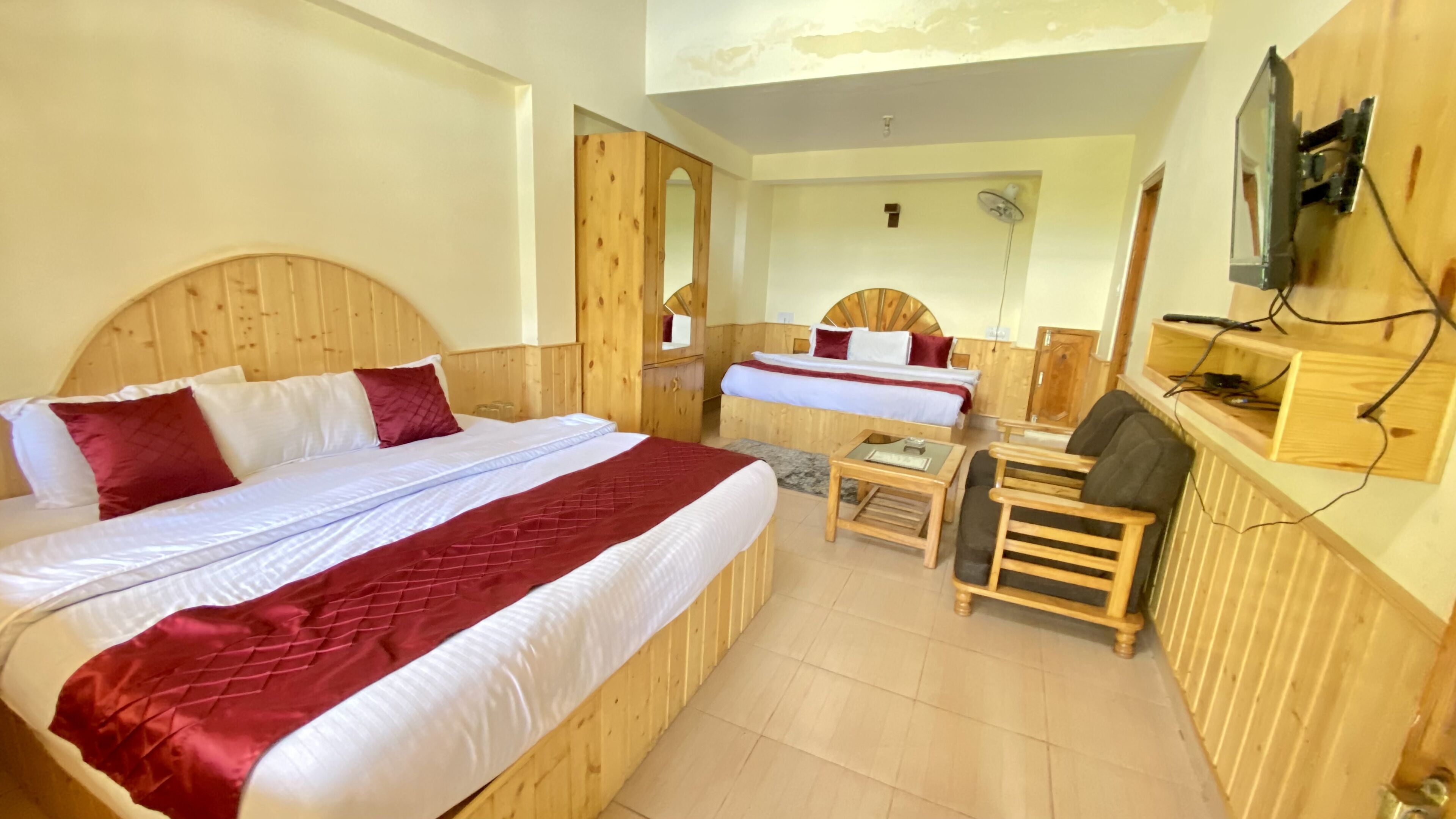 A wooden room with two beds, a small table, a chair, and a television mounted on the wall.