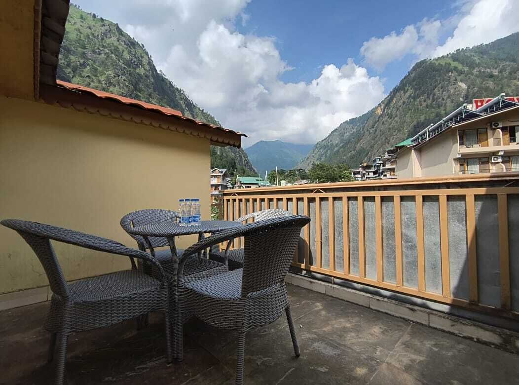 A balcony with wicker furniture and a table, overlooking a mountainous landscape with buildings in the background.