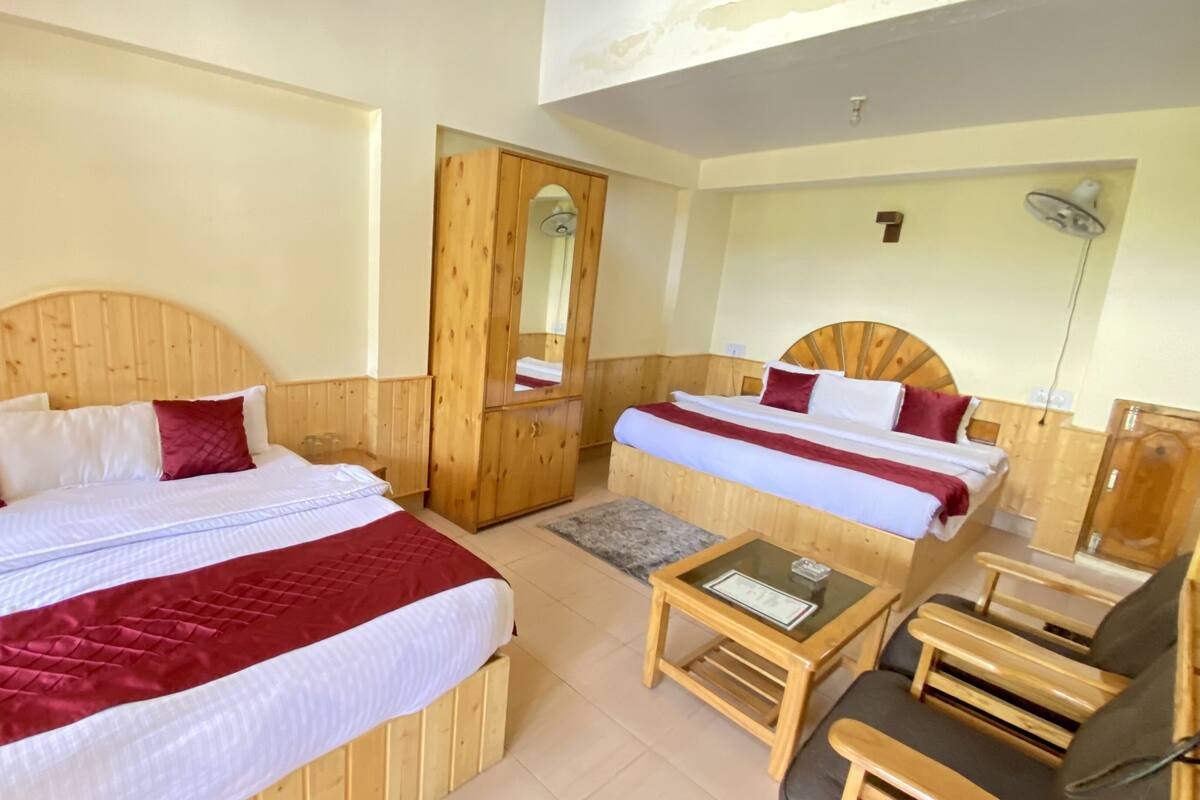 A hotel room with two wooden beds, a small table, a chair, and a mirror.