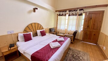 Un dormitorio con cabecera de madera, una cama con ropa de cama blanca y roja, una mesita de noche con un teléfono, una silla y una ventana con cortinas.