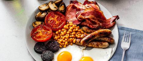 Un plato de comida para el desayuno con huevos, salchichas, tocino, tomates, frijoles y champiñones.