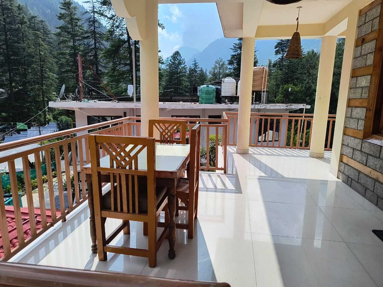 A covered outdoor area with a wooden table and chairs, a tiled floor, and a view of a mountainous landscape.