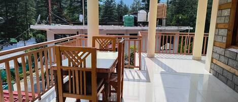 A covered outdoor area with a wooden table and chairs, a tiled floor, and a view of a mountainous landscape.