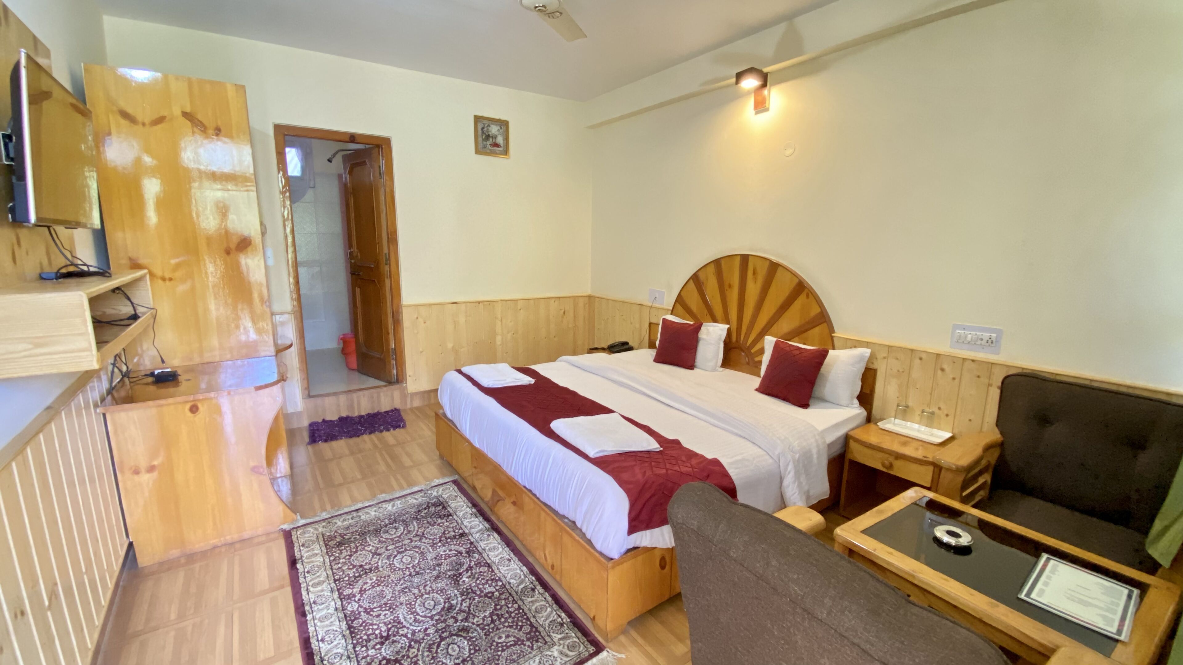 A wooden-furnished bedroom with a bed, bedside table, and a small seating area.