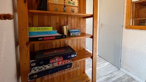 A wooden shelf unit with various board games and a door in the background. - Cozy Mini T2 in Barcelonnette - For 4, sunny balcony (Barcelonnette)